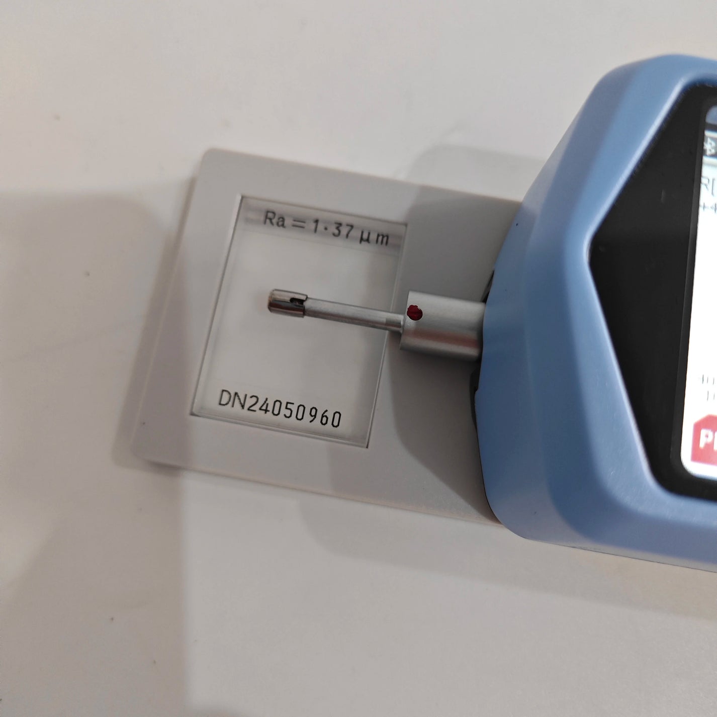 Probe measuring Ra roughness sample block beside portable tester screen